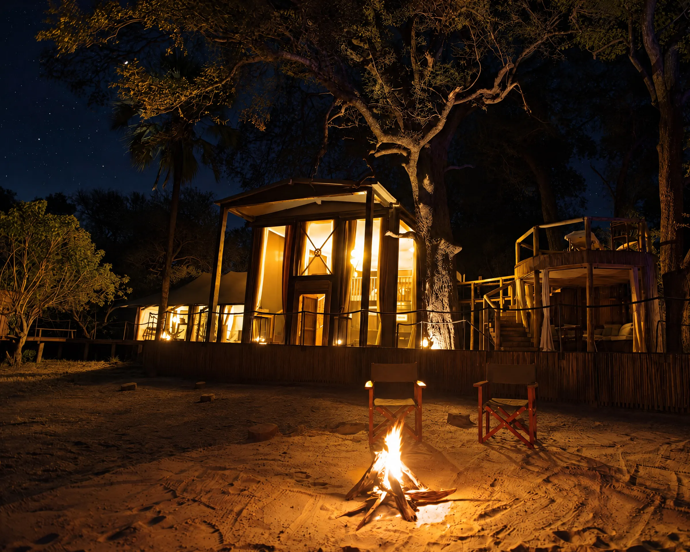 A villa at night, its windows lit, two chairs set by a campfire on the sand