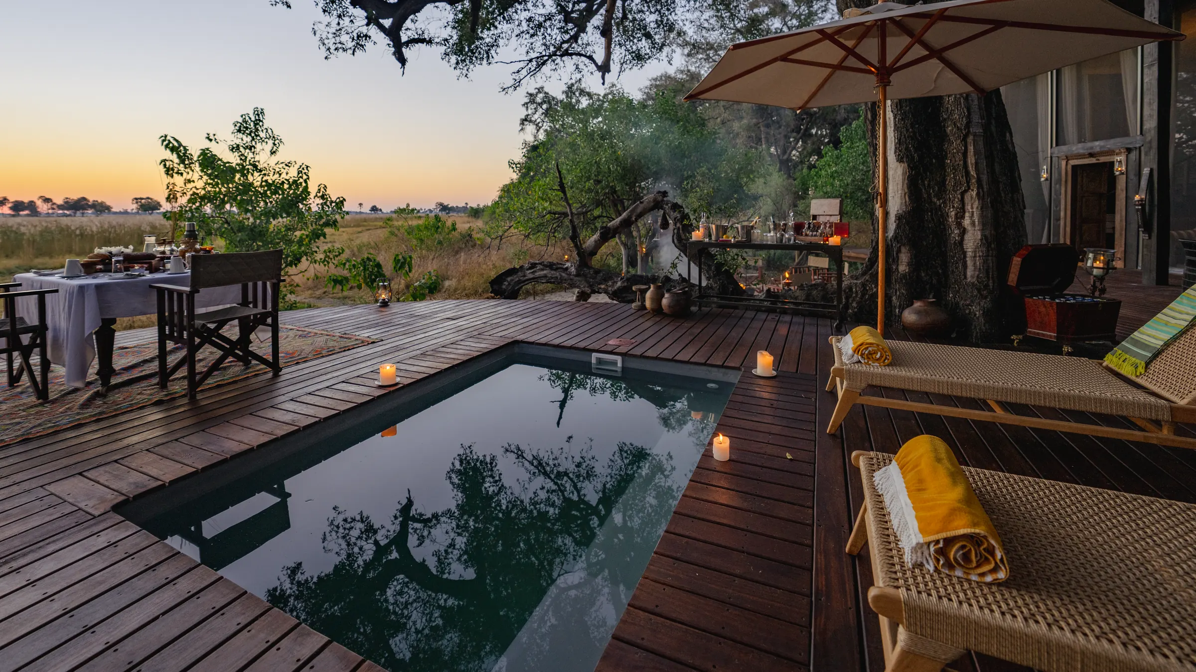 A villa deck at sunset, the plunge pool lit by candles, a table laid at the edge and the floodplain beyond