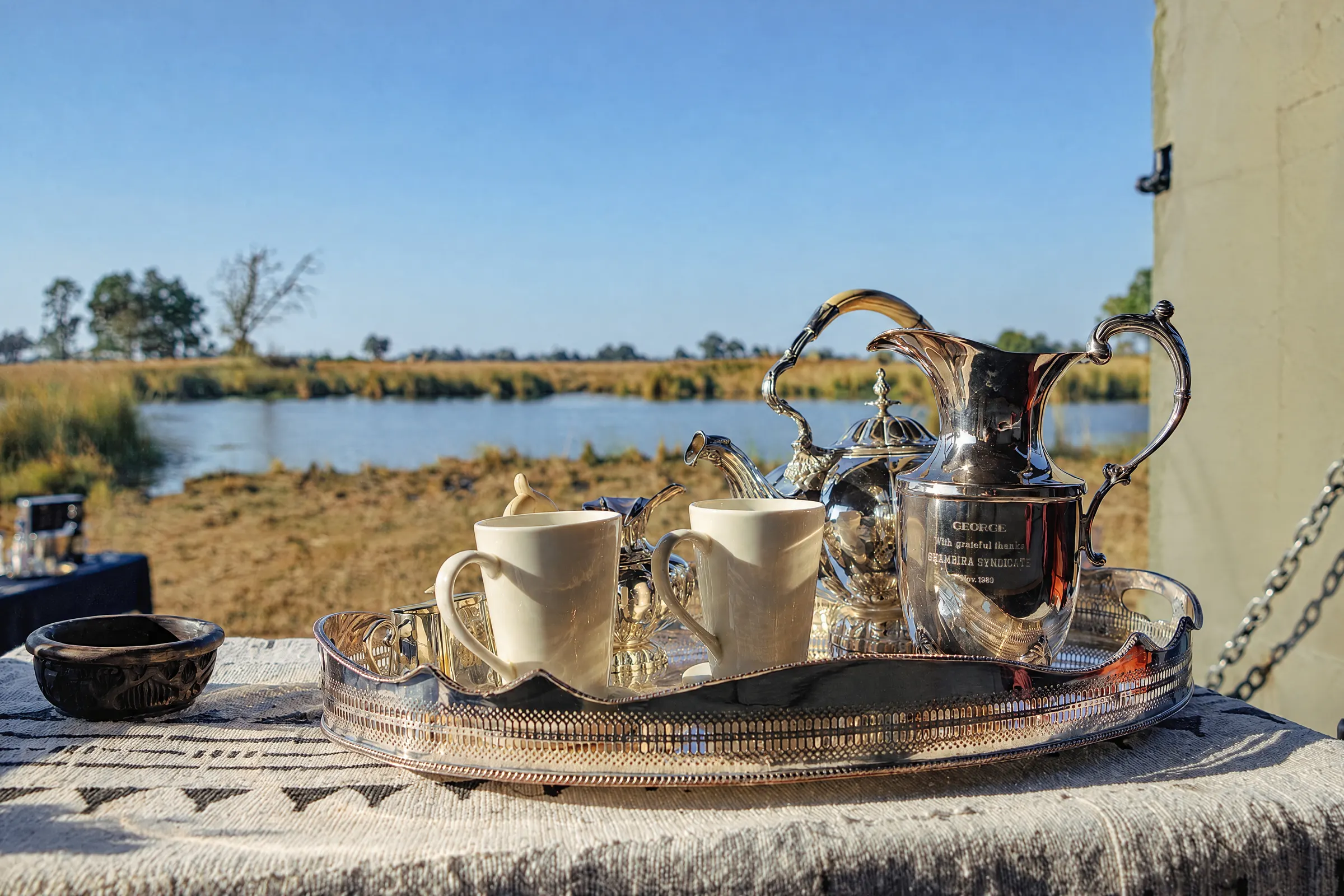 A silver tea tray with two cups on a table, the lagoon and the floodplain behind