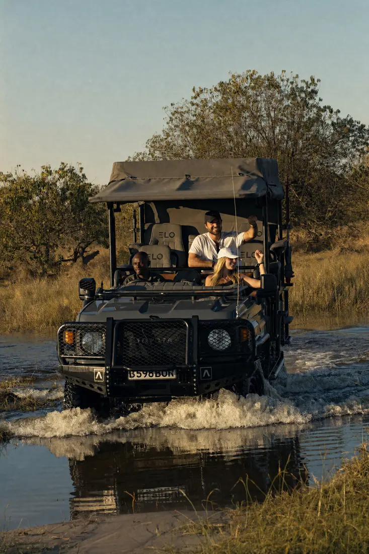 A game vehicle driving through the shallows, water spraying from its wheels