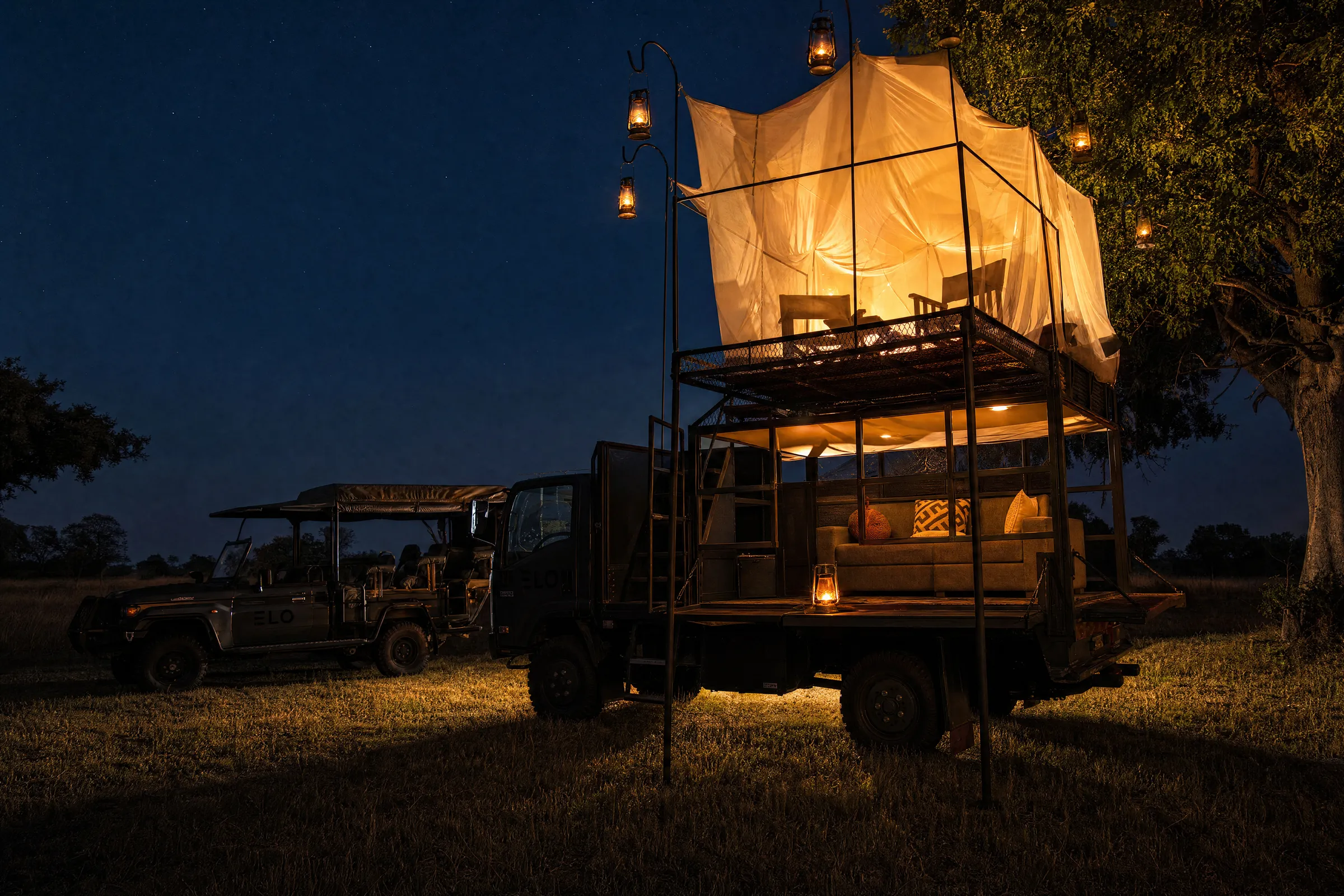 The sleep out truck at night, its bed lit under the netting and lanterns hanging from their poles, a game vehicle parked beside it