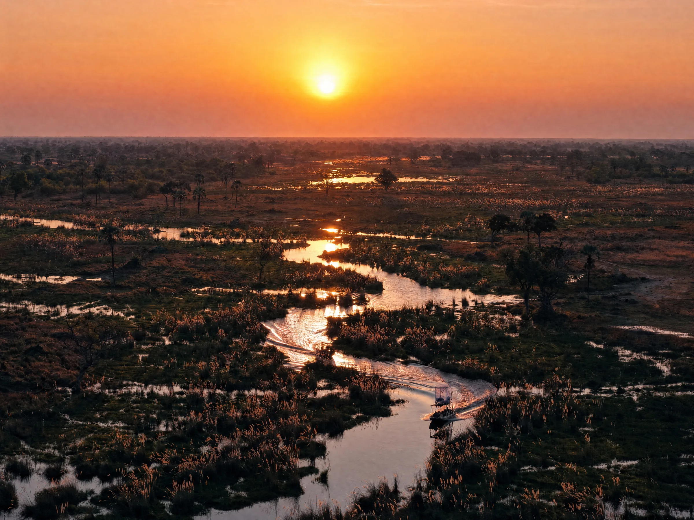 A boat leaving its wake along a winding channel at sunrise, seen from above