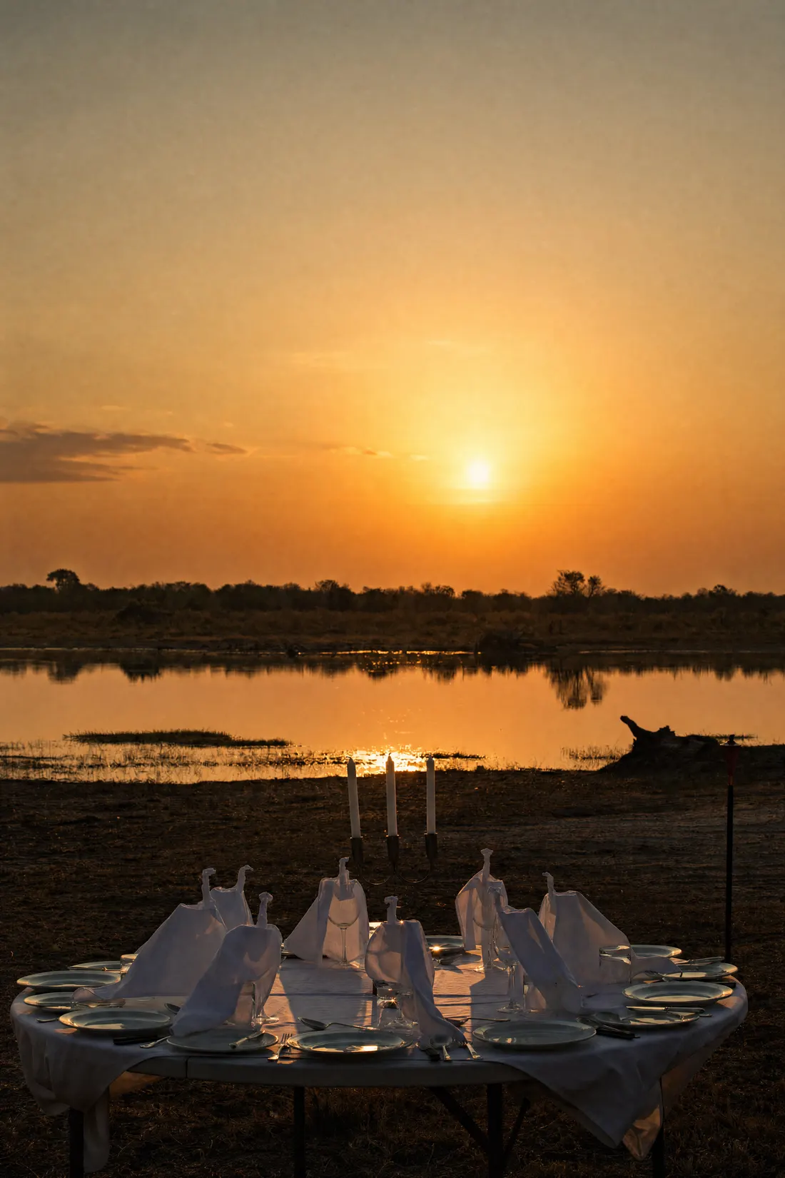 A round table laid by the lagoon, the sun setting over the water