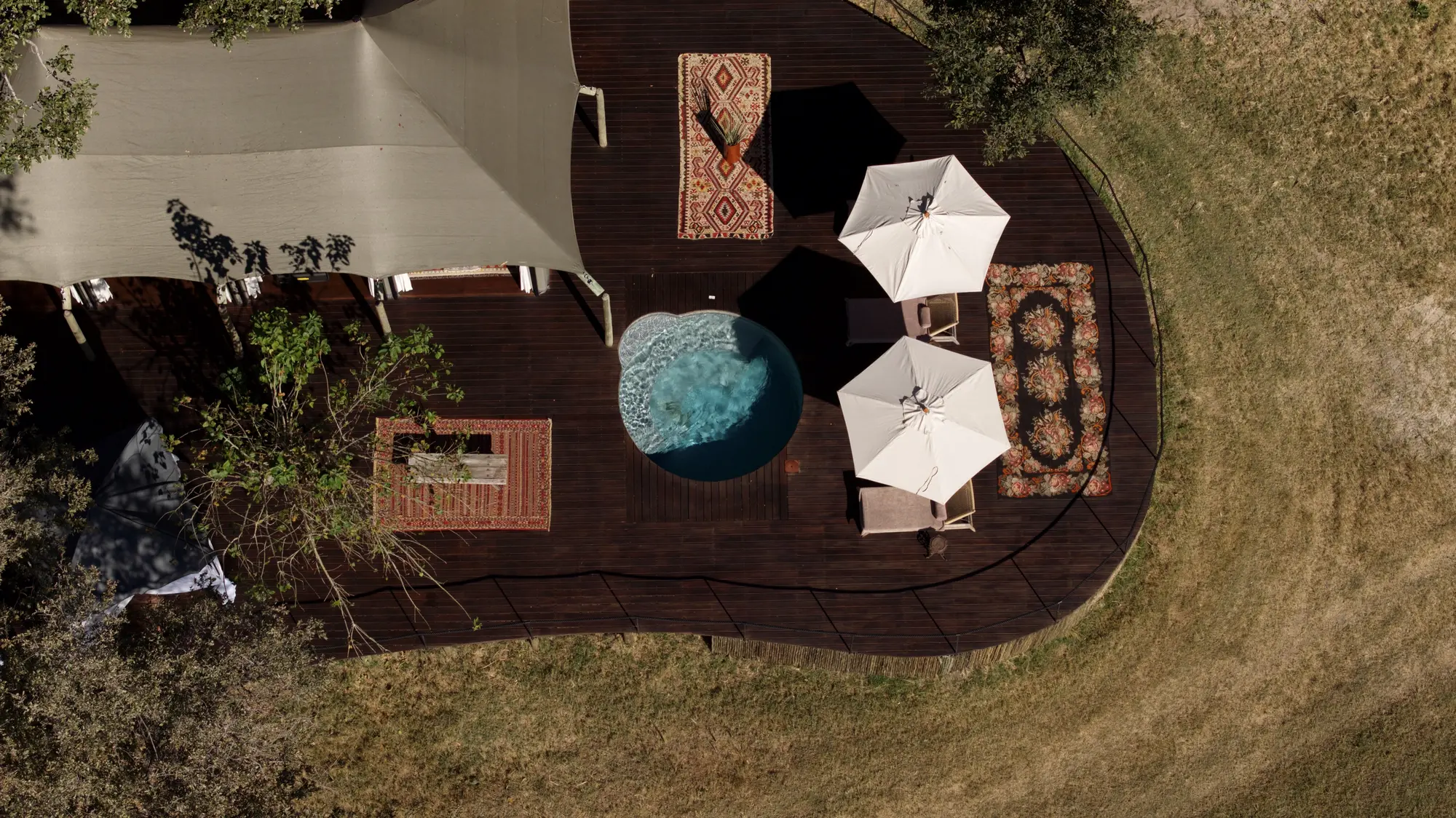 A family villa seen from straight above: its canvas roof, the deck with rugs and parasols and the round pool