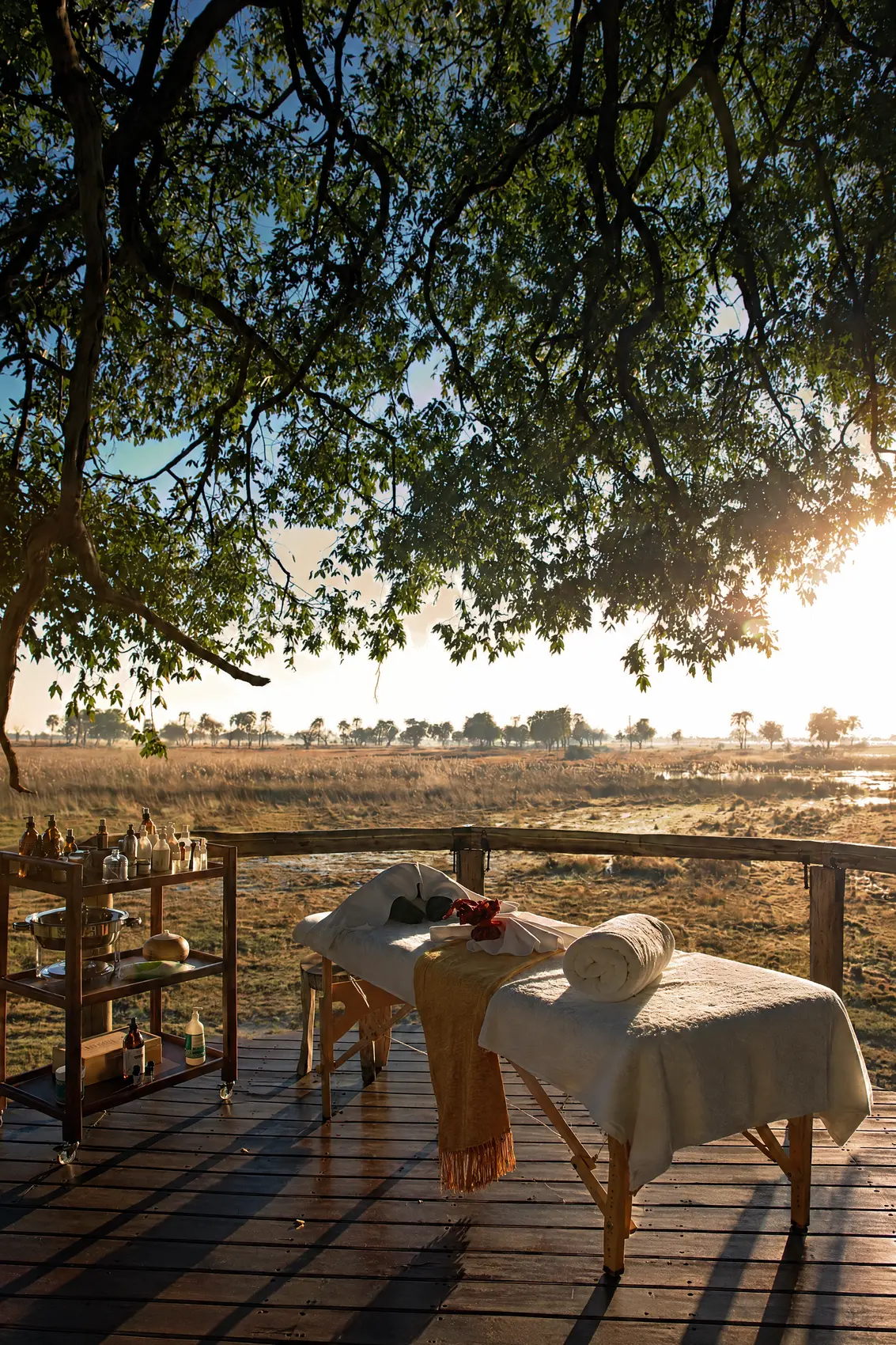 A massage table laid out on the deck under the trees, a trolley of oils beside it, at sunrise